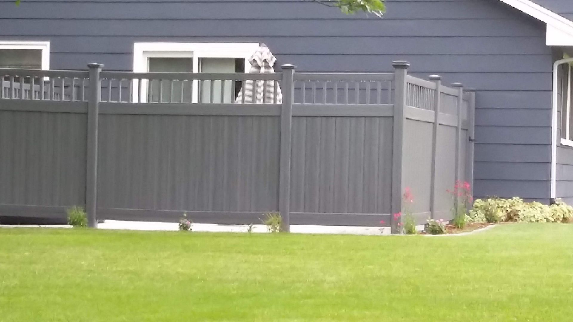 Backyard with gray fence, green lawn, and blue house wall behind it