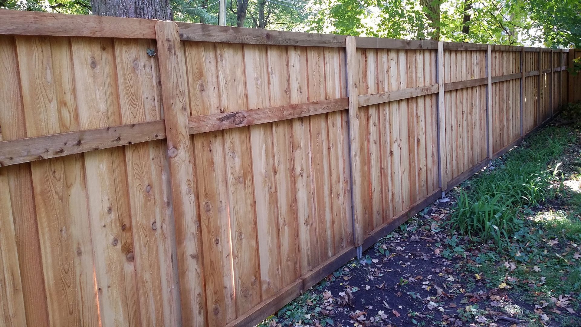 Wooden privacy fence along a grassy yard beside a wooded area