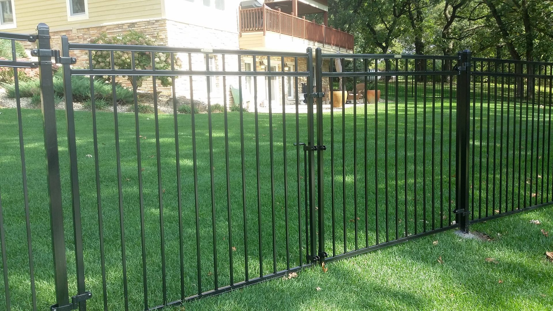 Black metal fence around a green lawn in front of a house