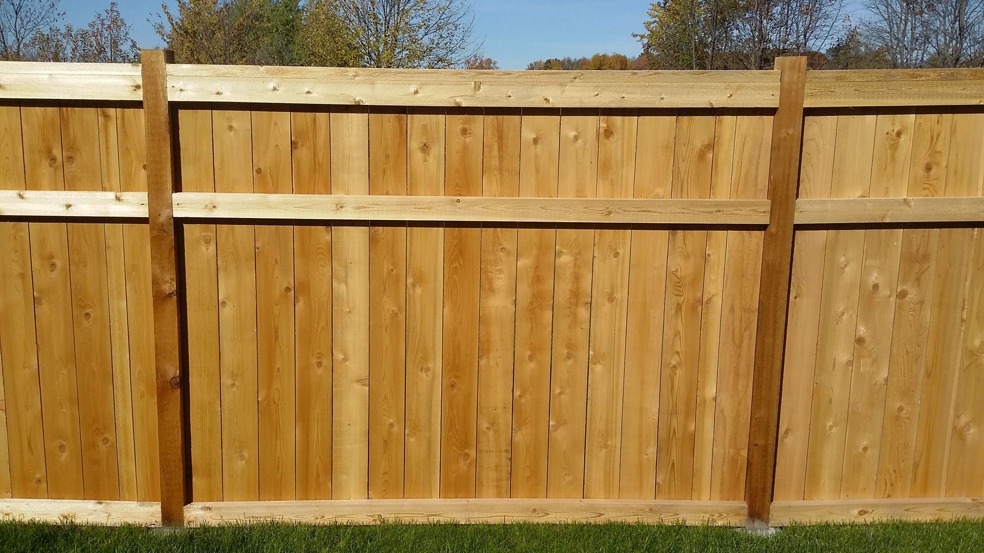 Wooden backyard fence with horizontal supports and grass at the base under a clear sky
