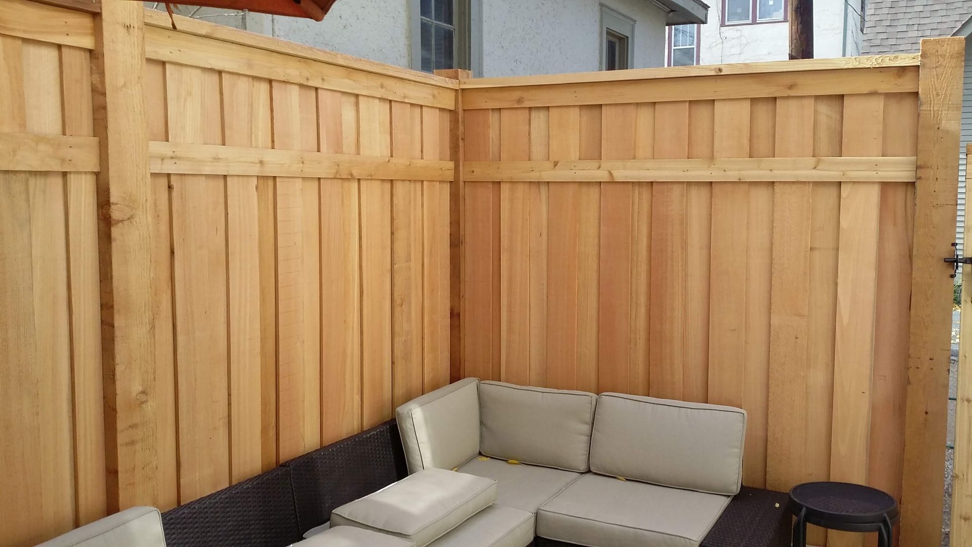 Patio corner with beige sectional seating against a light wood privacy fence.