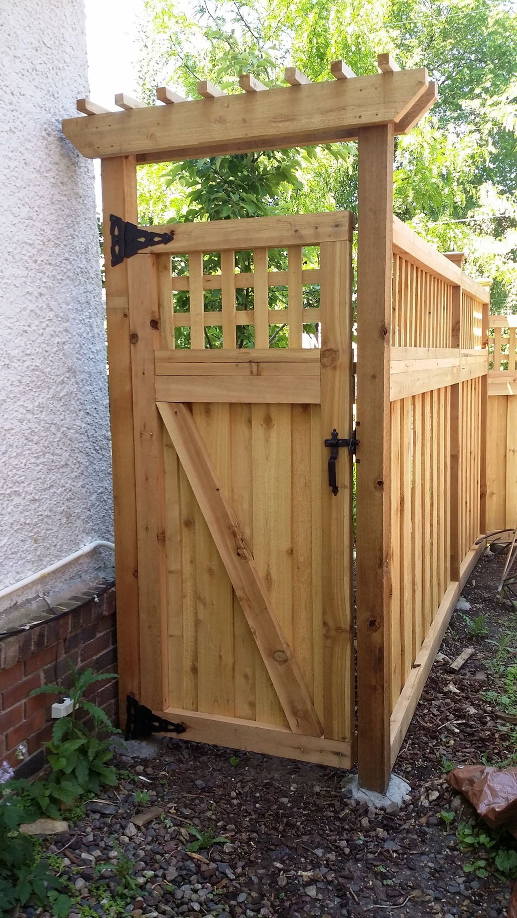 Wooden garden gate and fence beside a house, with lattice top and diagonal bracing.