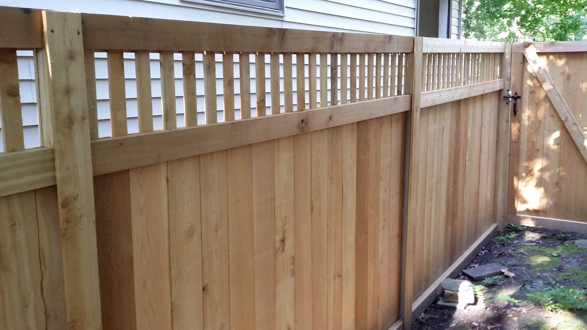 Wooden privacy fence with lattice top along a narrow backyard path in daylight