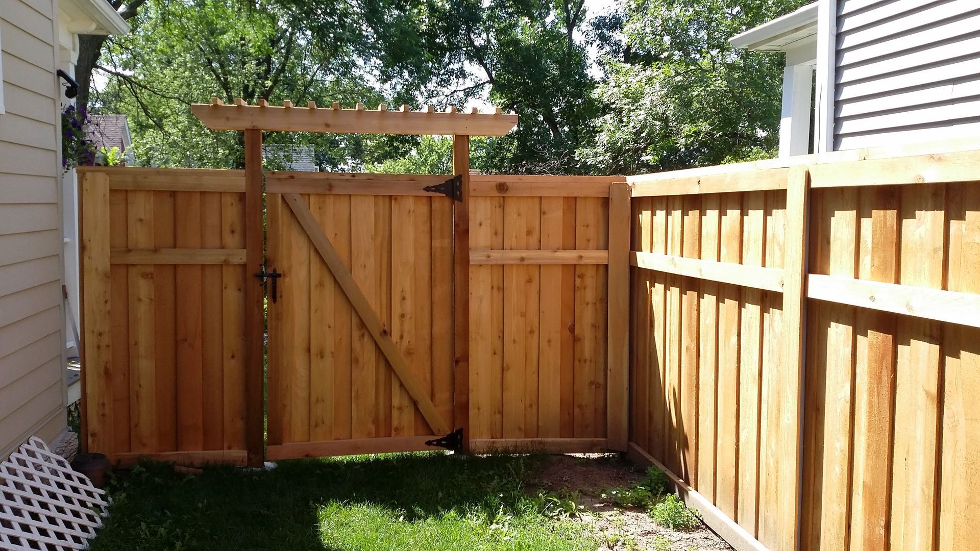 Wooden backyard gate and fence between two houses, with grass and trees beyond.