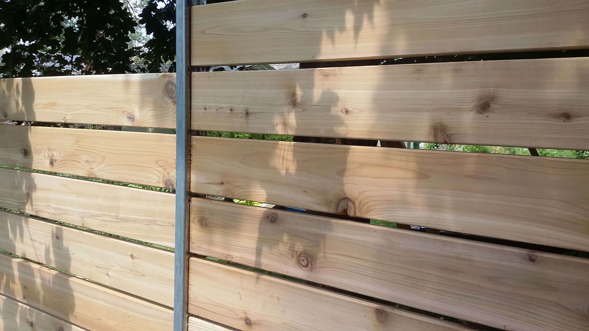 Wooden fence with horizontal boards and a dark metal post in sunlight.