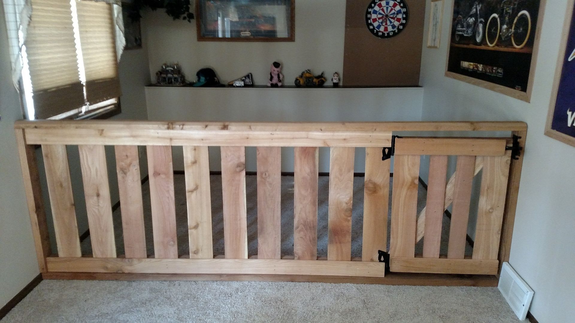 Wooden baby gate blocking a doorway in a carpeted room, with a dartboard on the wall.