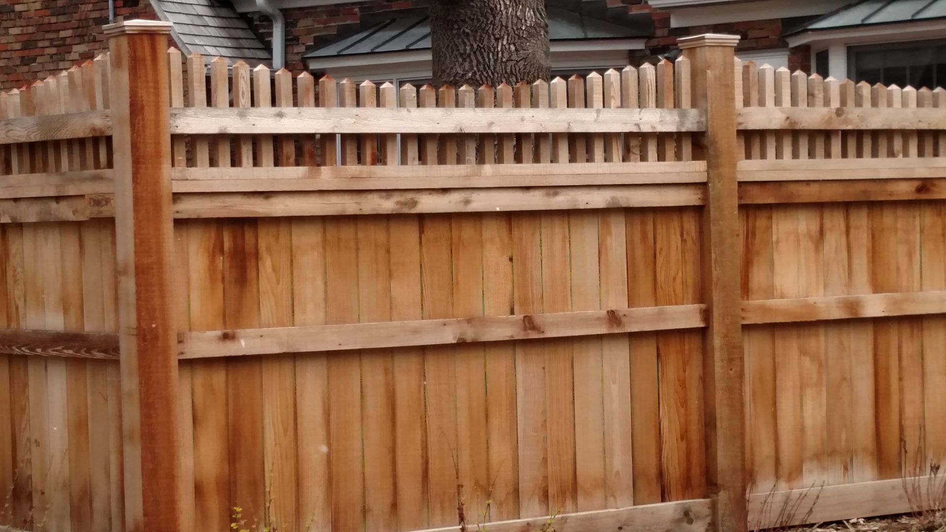 Wooden privacy fence in a backyard, with vertical slats and a weathered finish.