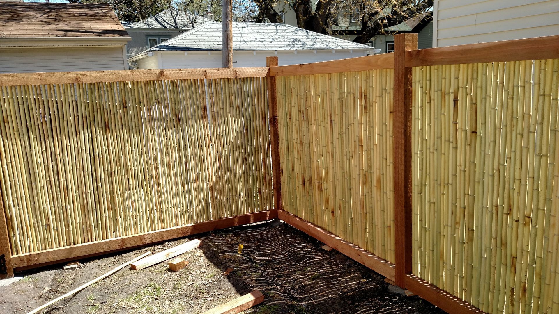 Bamboo privacy fence enclosing a small dirt yard with wood framing and a tree in the corner
