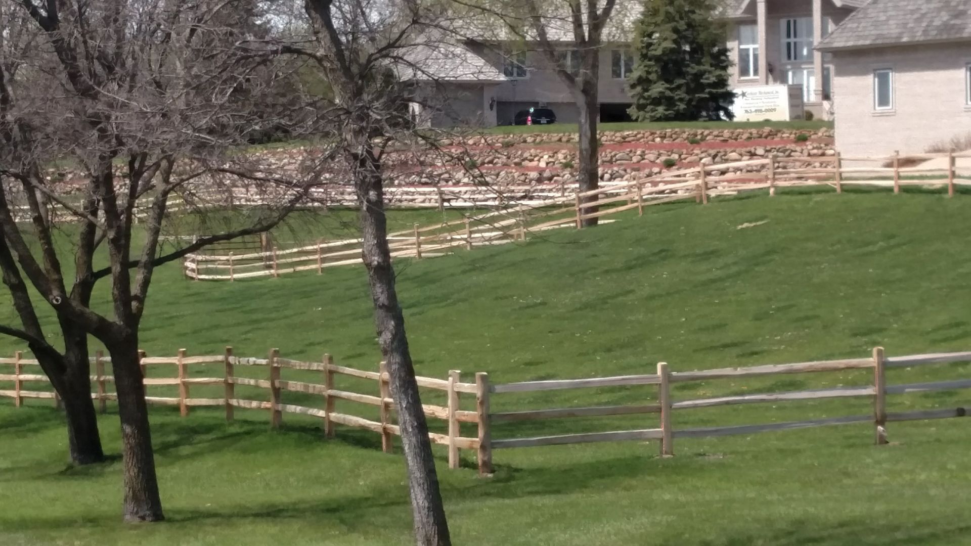 Grassy fenced pasture with leafless trees and houses in the background