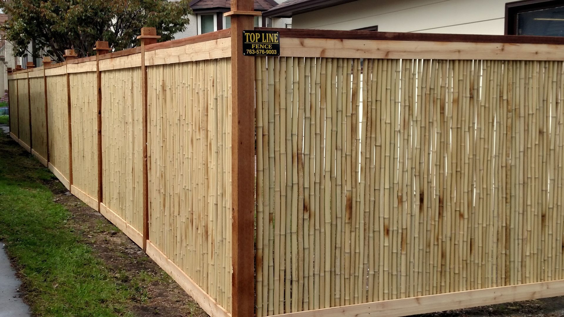 Wooden privacy fence along a wet sidewalk beside a house, with a corner gate and dark red posts.