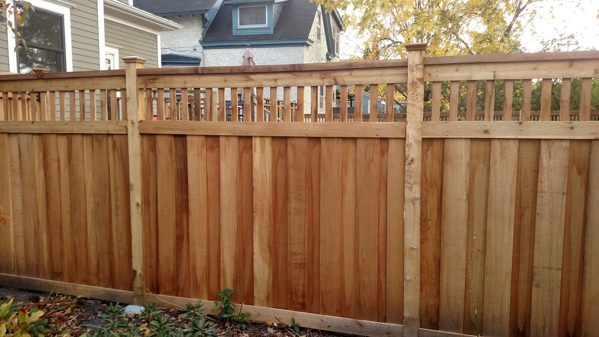 Wooden backyard fence with vertical slats and a narrow gate, seen in front of a house