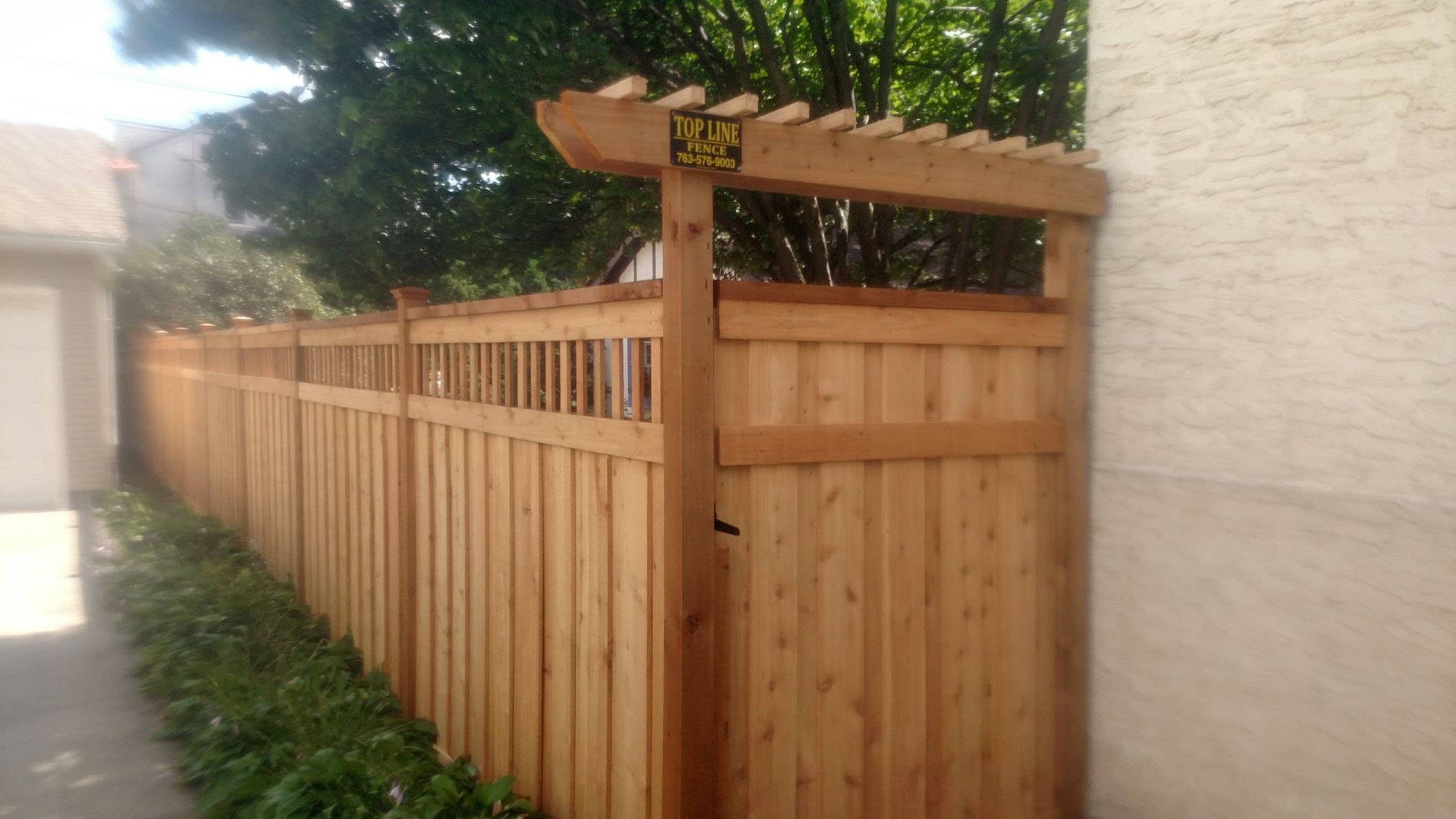 Wooden privacy fence along a side yard, with a tall gate and lattice top beside a stucco wall.