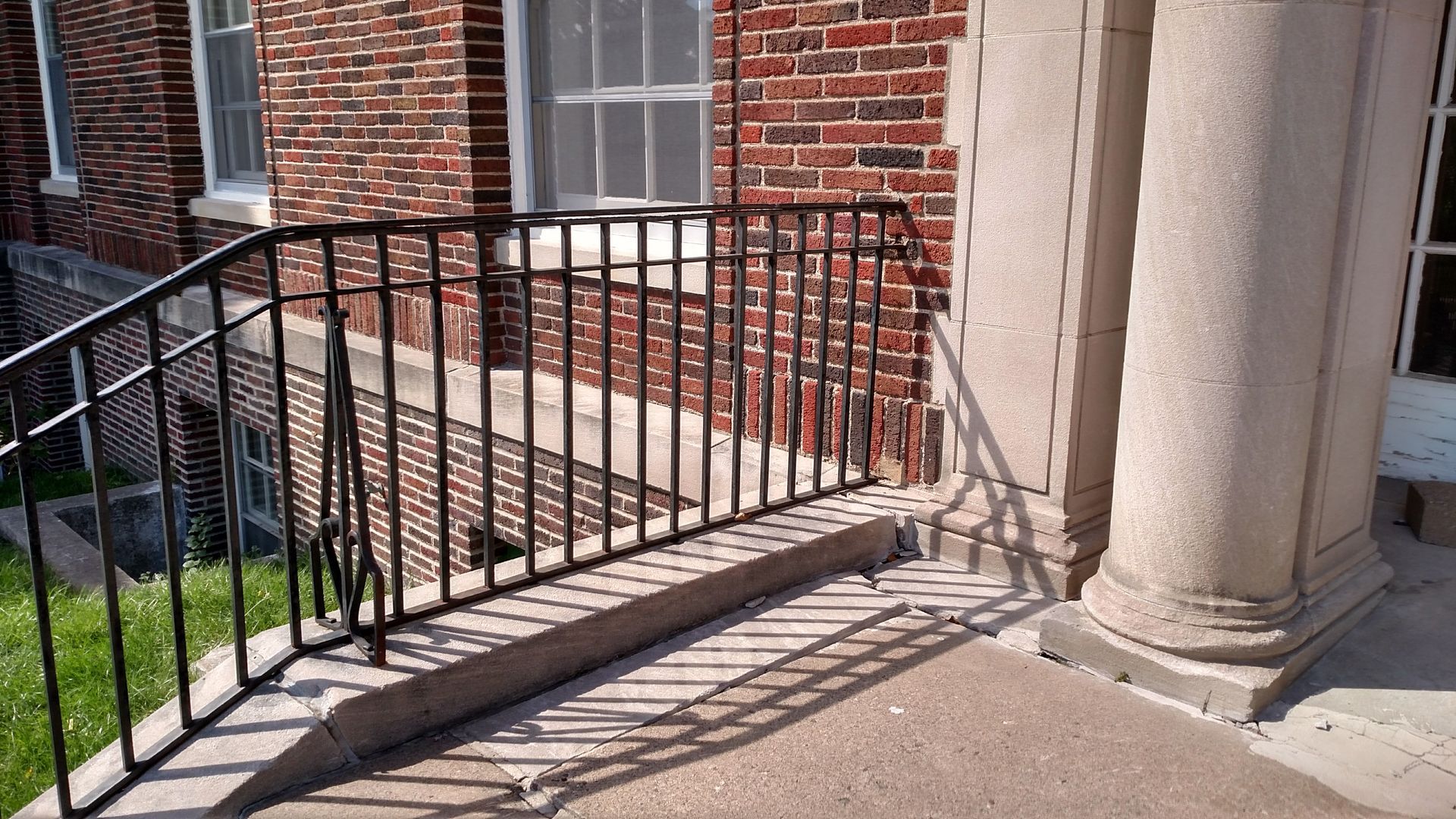 Black metal accessibility ramp beside brick building steps and columns.