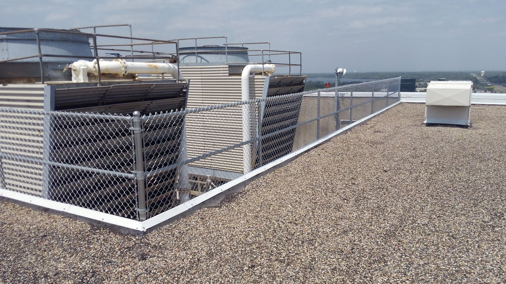 Rooftop HVAC equipment and gravel surface with metal fencing and city skyline in the background