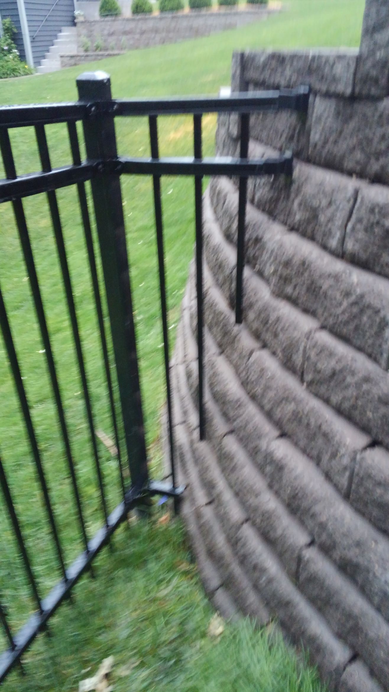 Black metal fence corner beside a tan stone retaining wall over grass