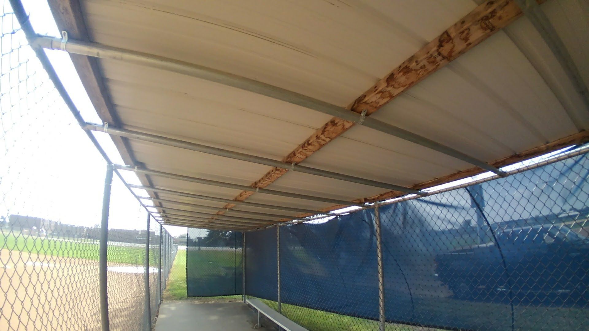 Covered walkway with blue netted sides and a metal roof beside a grassy field