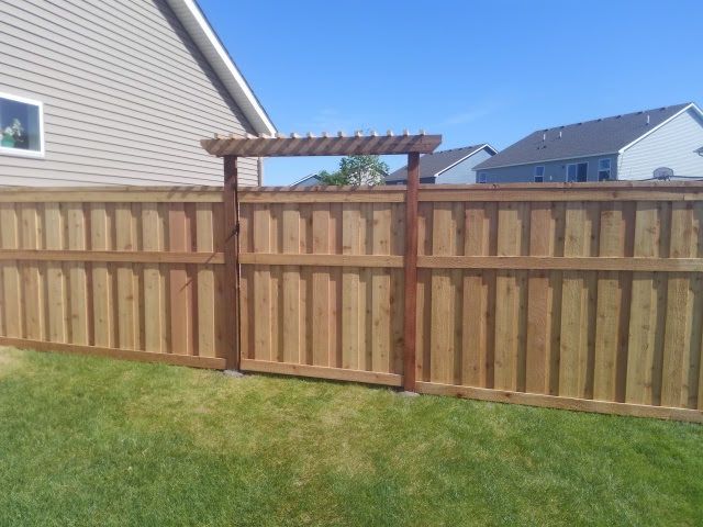 Wooden backyard fence with gate and pergola trellis over a grassy lawn, with houses in the background