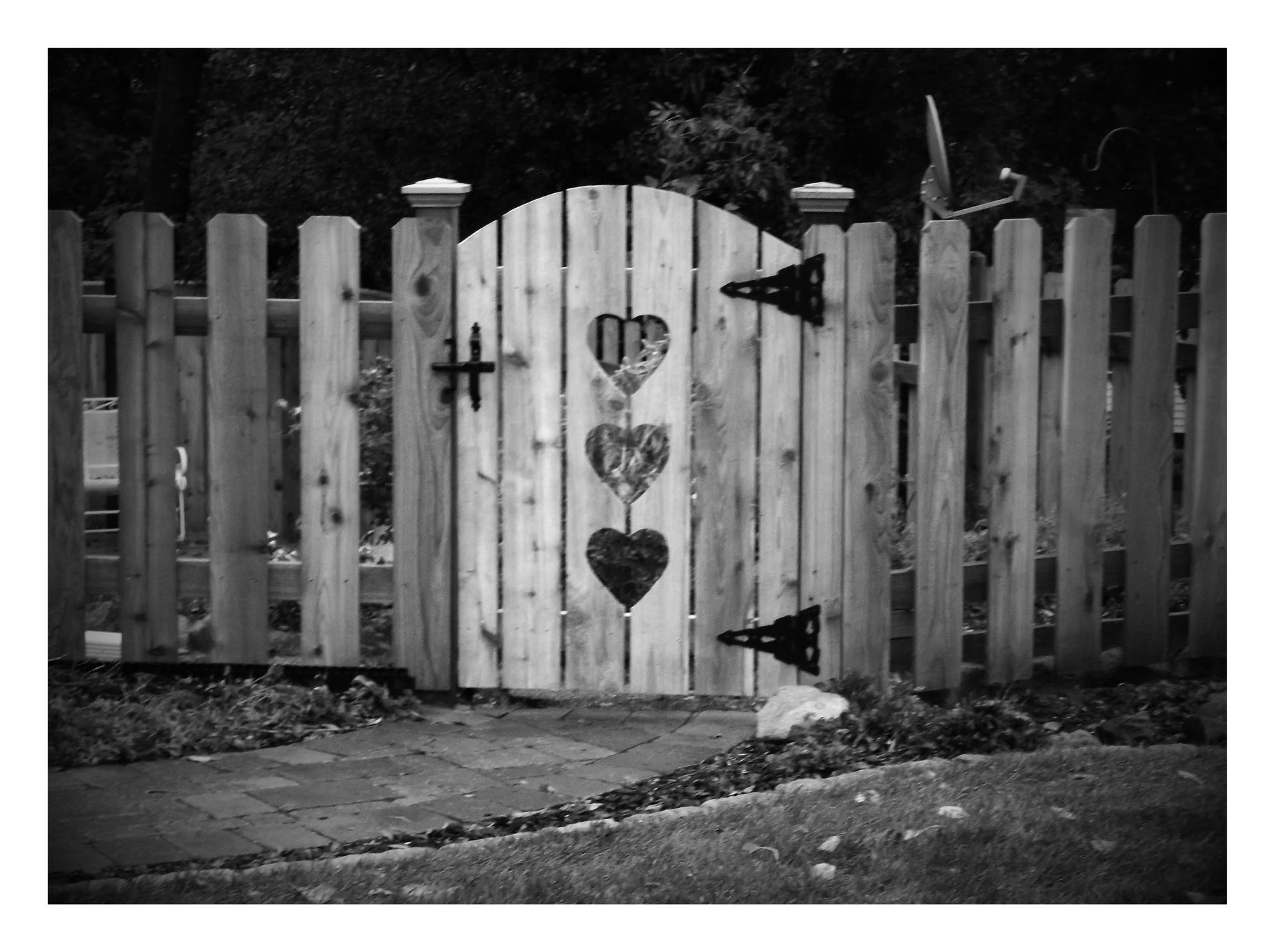 Black-and-white photo of a white wooden gate with two heart cutouts in a picket fence.