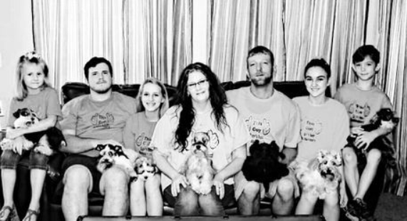 Black-and-white family portrait of seven people seated on a couch with several small dogs in their laps