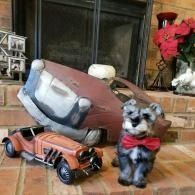 Small dog figurine with red bow beside an overturned chair and toy car on a brick hearth