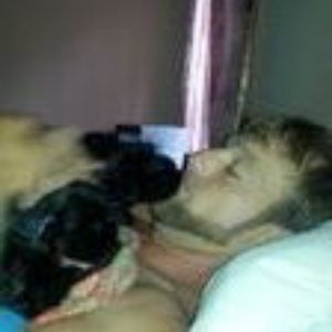 Person lying in bed holding a black puppy close to their face
