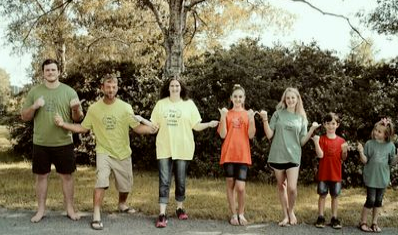 Seven people posing for a picture with trees in the background.