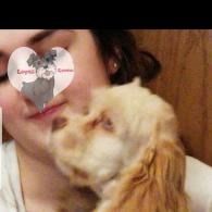 Small cream-colored dog licking a person’s cheek; a heart sticker covers part of the face.