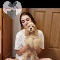 Young woman holding a fluffy tan dog indoors in front of wooden doors.