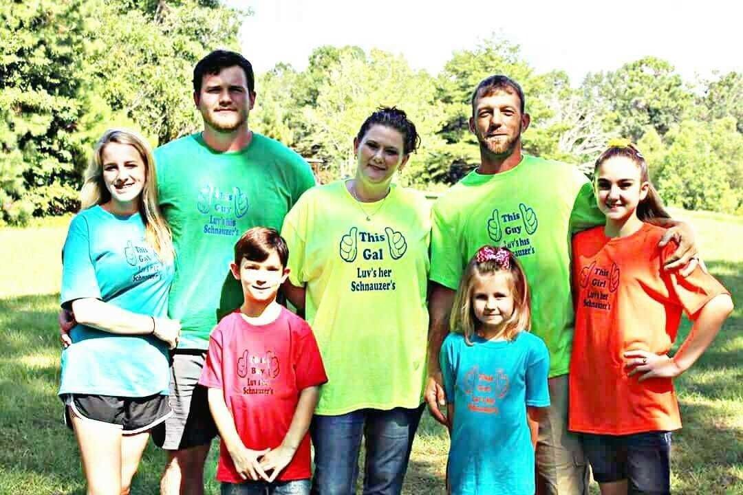 Seven people standing together outdoors in bright shirts, smiling in a sunny area.