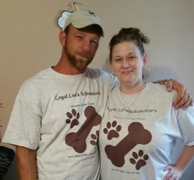 Two people in white T-shirts with brown paw prints pose indoors, smiling