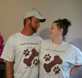 Two people in white T-shirts with dog paw prints smiling at each other indoors