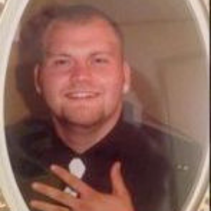 Smiling man in a dark shirt, seen in an oval-framed portrait.