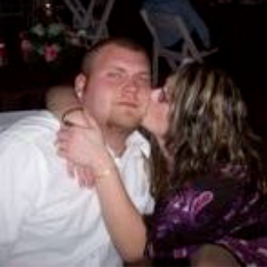 Two people embracing at a dimly lit area, with one person kissing the other's cheek.