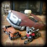 Two stuffed dogs on a couch beside an orange toy jeep and a tipped red toy vehicle