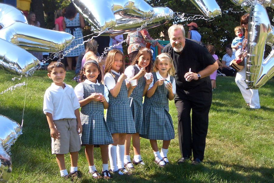 A group of children are posing for a picture with a man in a black shirt