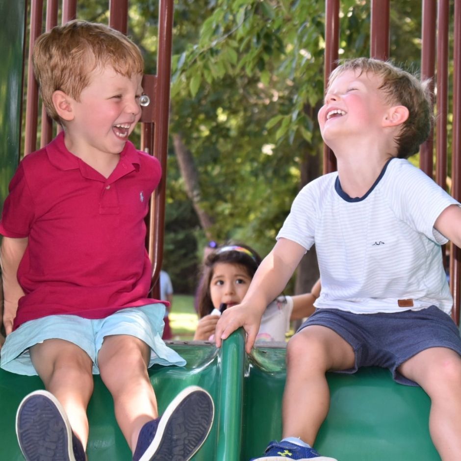 Two young boys are sitting on a slide and smiling