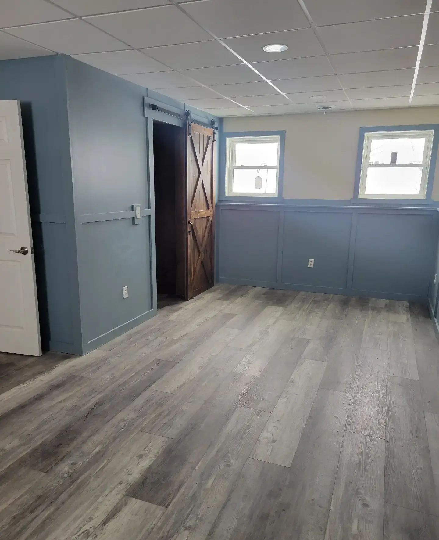 Empty room with gray wood-look floor, blue walls, and two small windows