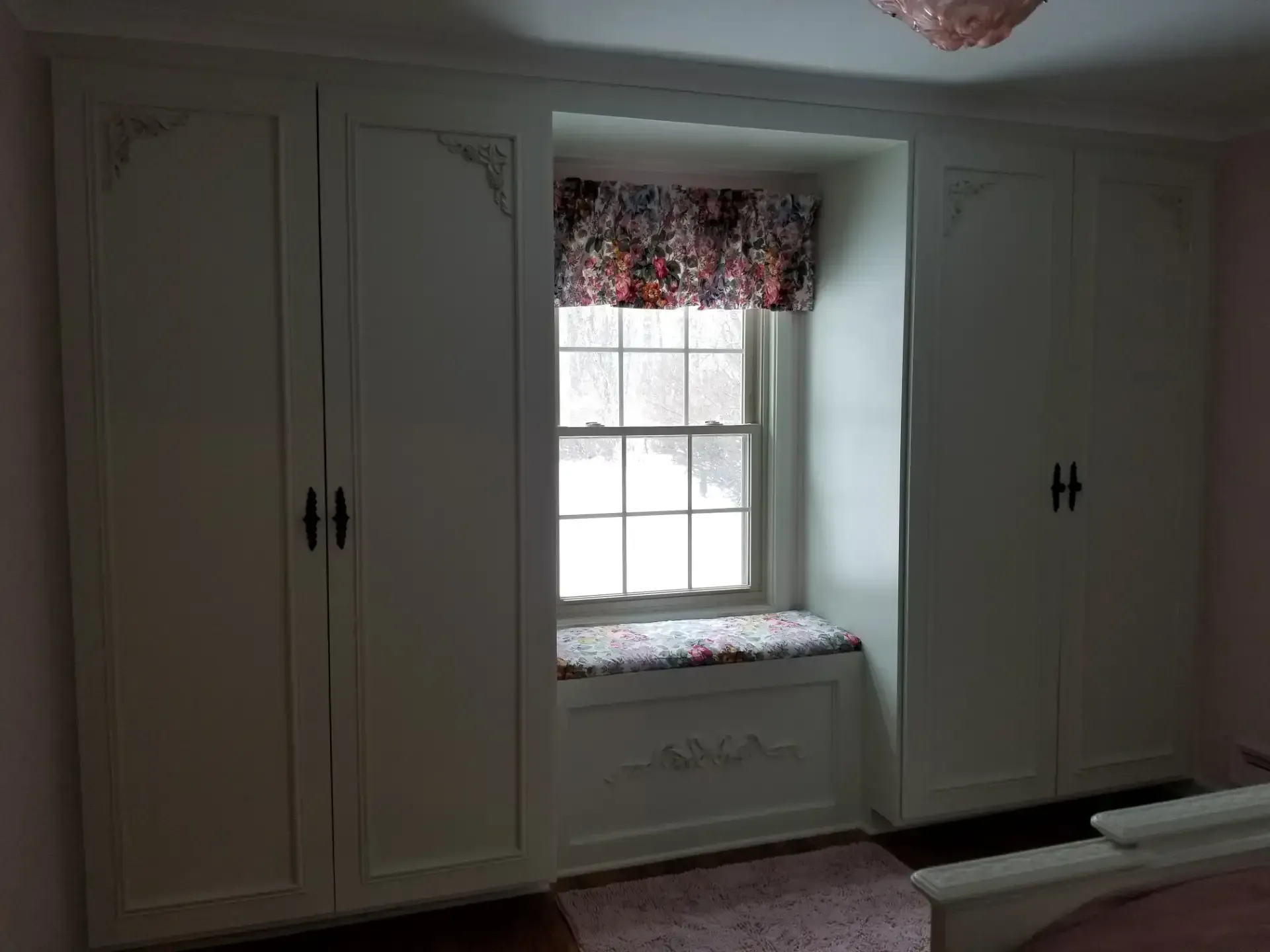 Built-in white cabinets flanking a window with a floral valance and seat.