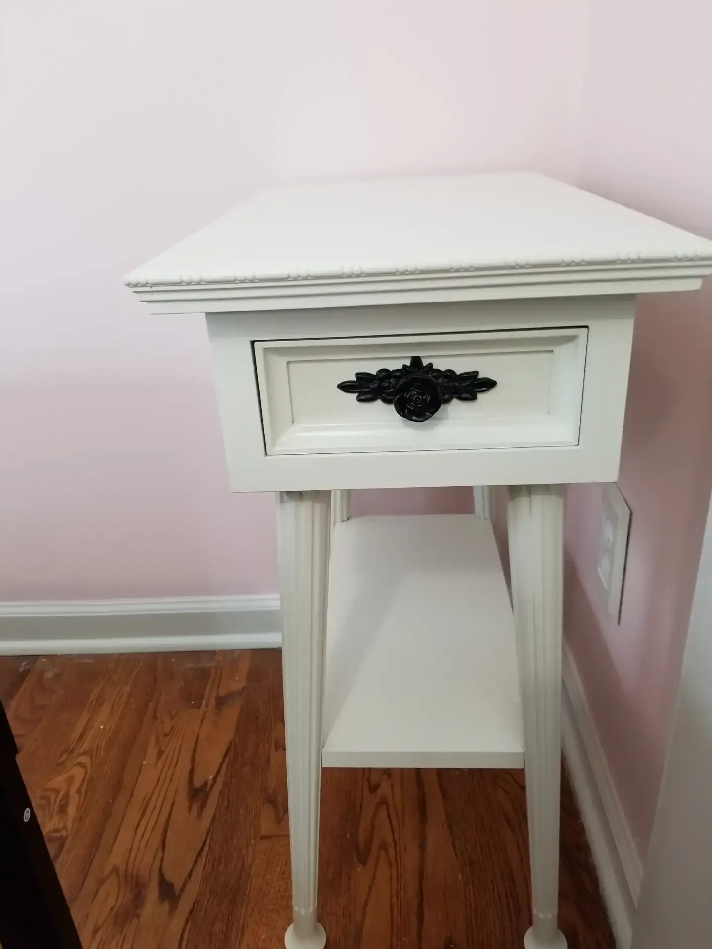 White painted nightstand with a drawer, shelf, and ornate black handle.