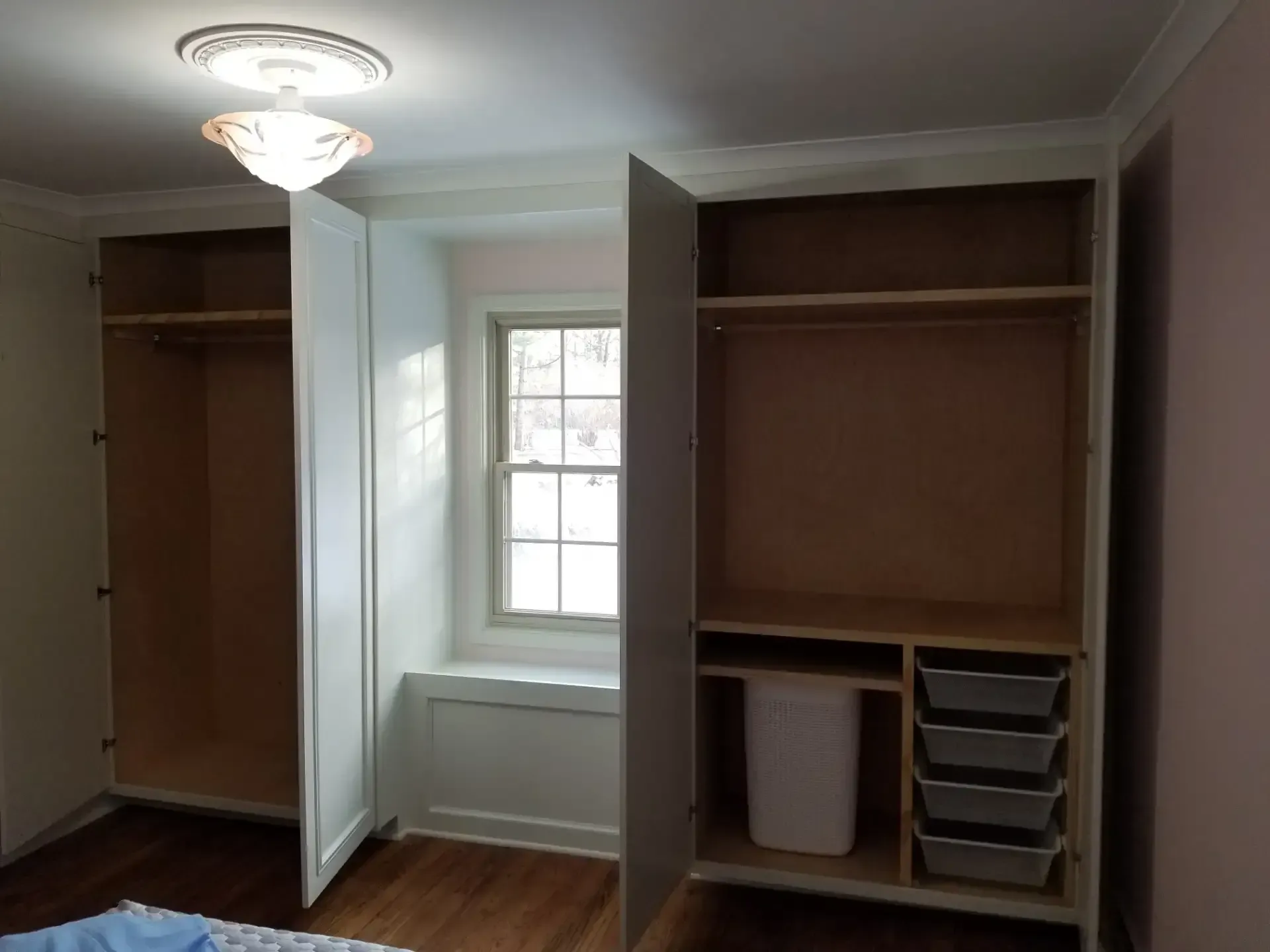 Built-in bedroom closet with open doors, wooden shelving and hanging rods. Includes a window and a storage unit.