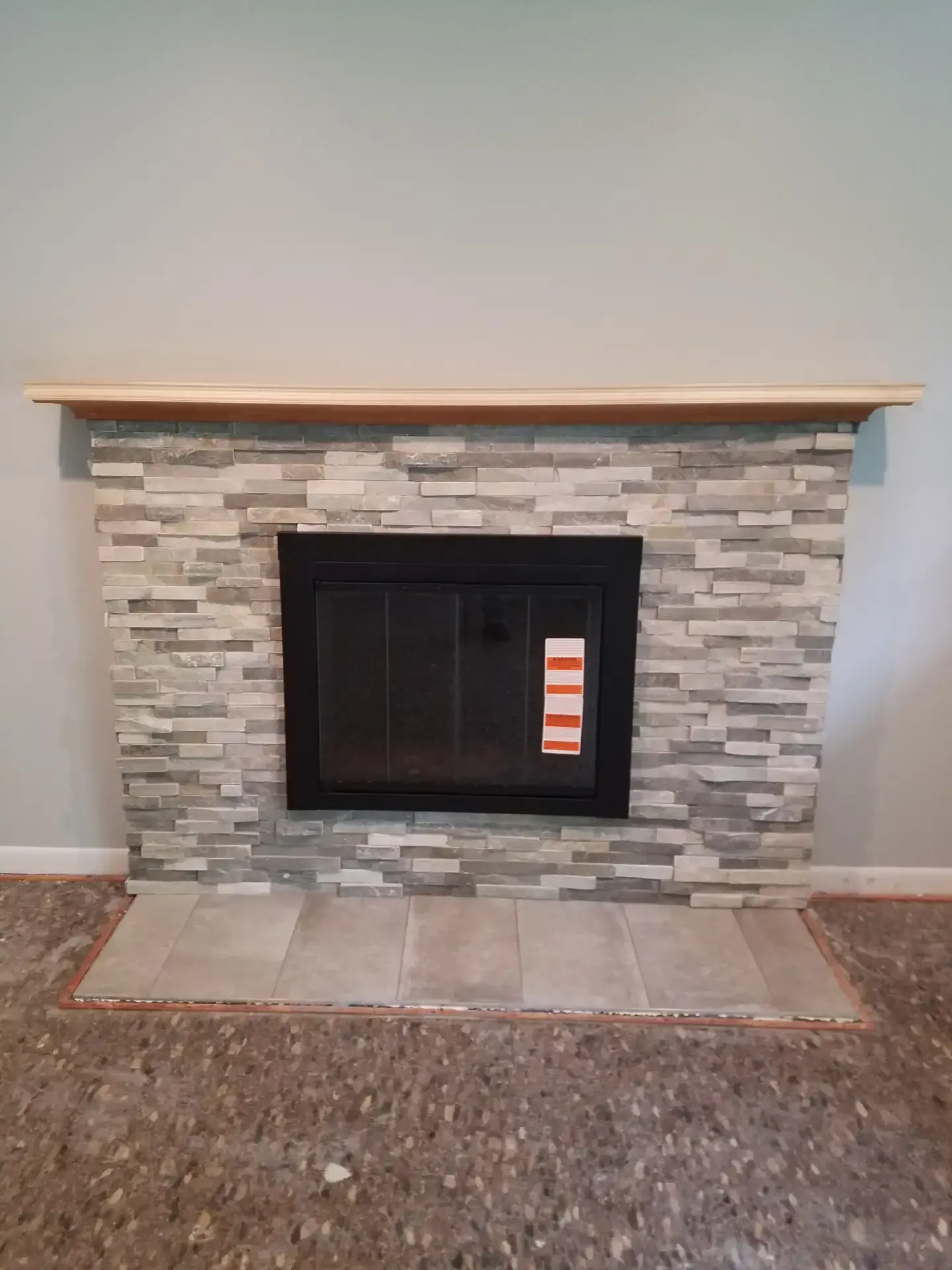 Fireplace with gray stacked stone, black firebox, and a wood mantel. Gray tile hearth.
