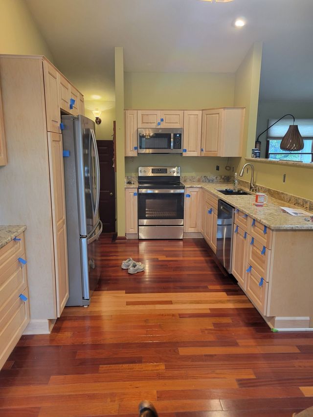 Kitchen renovation in progress: new light wood cabinets, stainless steel appliances, dark wood floors.