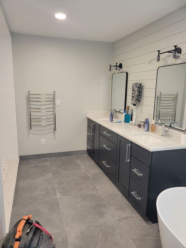 Bathroom with double vanity, gray cabinets, gray tiled floor, and heated towel rack.