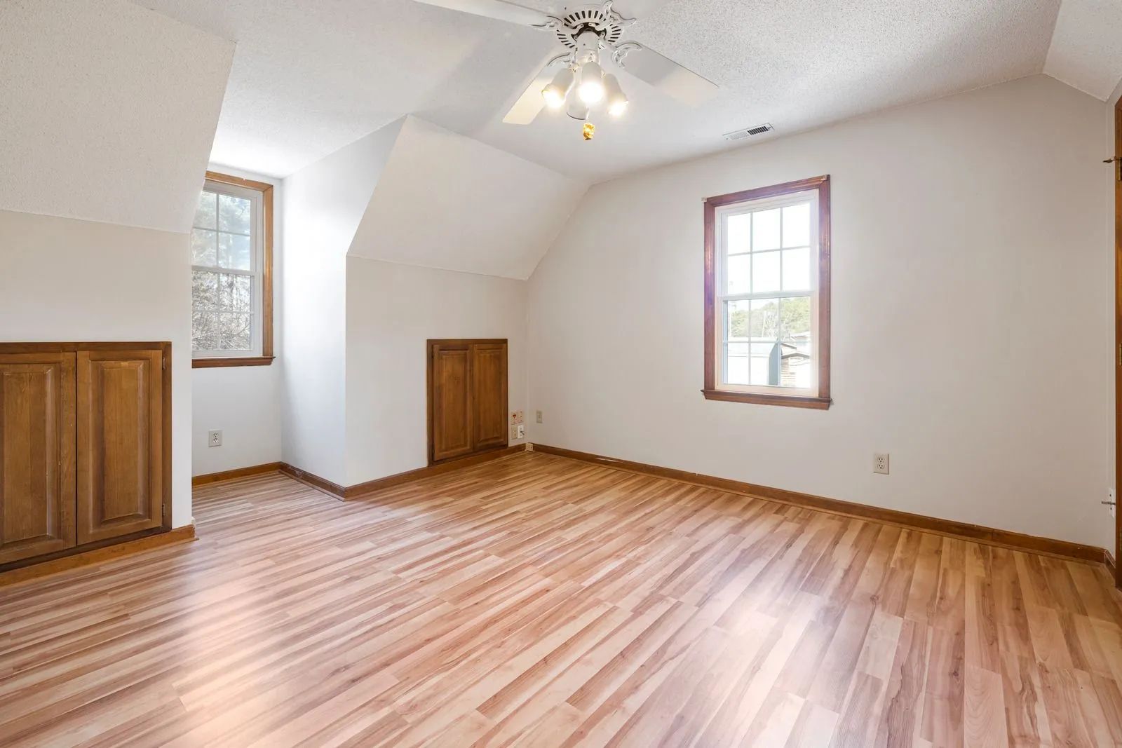 Empty room with hardwood floors, white walls, two windows, and ceiling light fixture