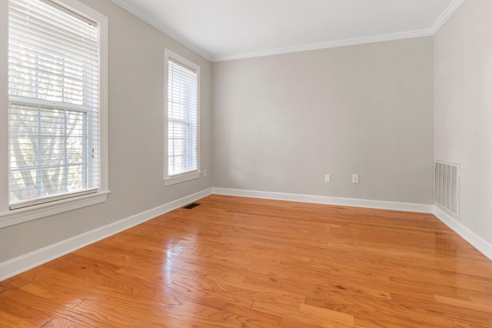 Empty room with hardwood floors, beige walls, and two windows with white blinds