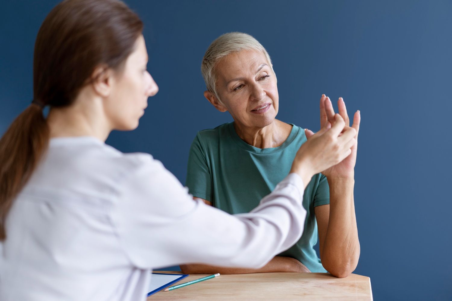 Clinician gesturing while speaking with a patient in a teal shirt at a table