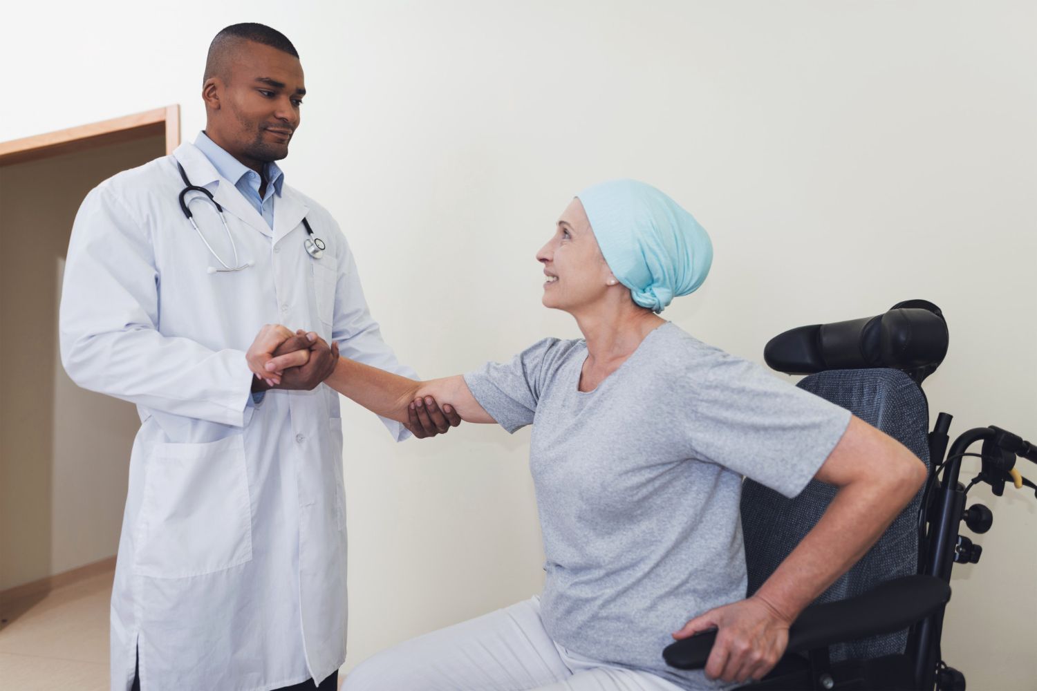 Doctor talking with a patient in a wheelchair, shaking hands in a clinic room.