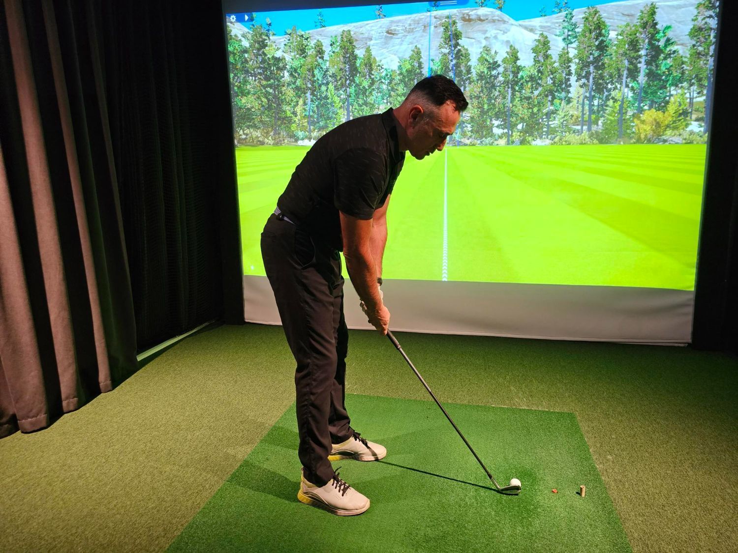 Golfer practicing a putt indoors on a virtual golf simulator with a green fairway backdrop