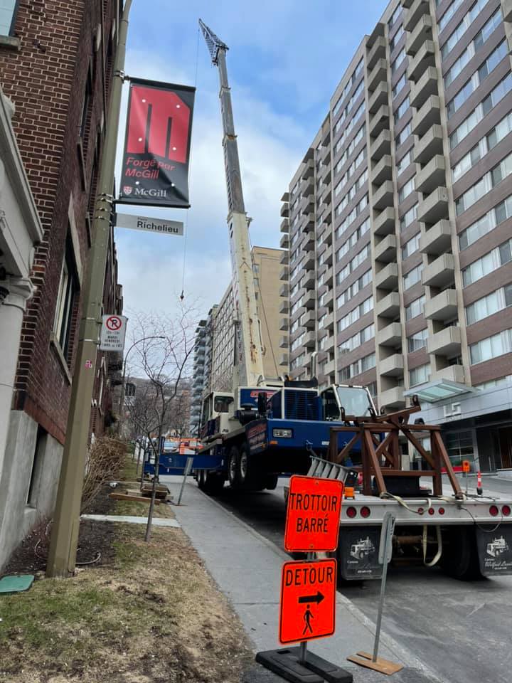 Une grue est posée sur le bord de la route, devant un grand immeuble.