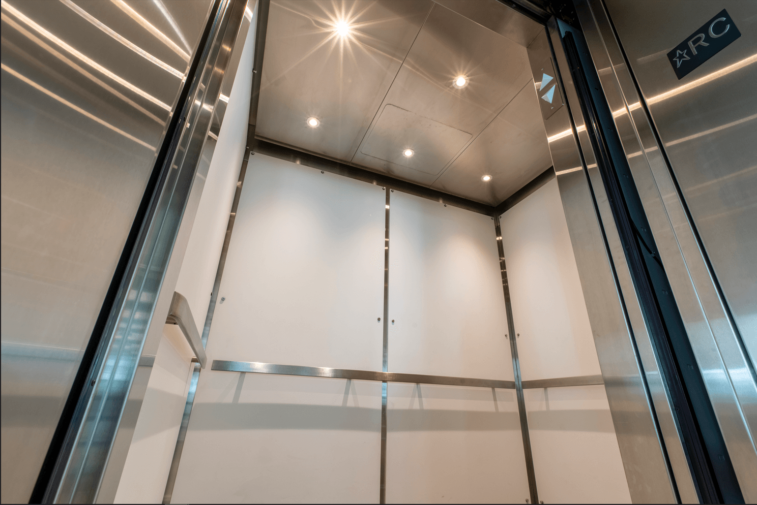 L'intérieur d'un ascenseur avec des parois en acier inoxydable et une porte vitrée.